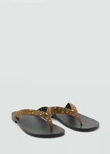 Sandalias planas de dedo tipo thong, confeccionadas en piel de serraje color marrón, con tiras decoradas con tachas y ojetes metálicos dorados.