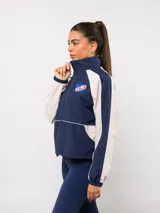 Campera deportiva Umbro del Club Nacional de Football, con diseño de bloques de color en azul marino y blanco. Presenta cuello alto, cierre frontal completo, bolsillos laterales y el escudo del club junto al logo de la marca en el pecho.
