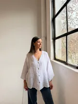 Camisa blanca de lino, con cuello en V, cierre frontal de botones y mangas amplias de corte holgado.