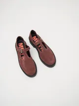 Zapatos tipo guillermina de gamuza color bordó, con diseño de tira en T, cierre con hebilla metálica y costuras a la vista en hilo blanco. Poseen una suela de plataforma de goma negra de 4 cm.