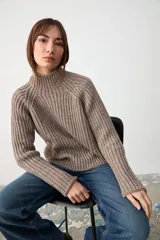 Sweater de punto acanalado en color gris topo, con cuello alto y mangas largas raglán. Presenta un diseño de corte holgado y una pequeña etiqueta decorativa en el lateral.