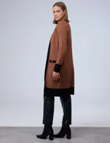 Cardigan largo tejido color marrón con ribetes negros en contraste, bolsillos delanteros y mangas largas.