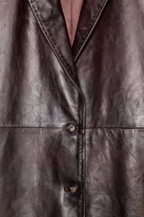 Abrigo largo de piel color marrón oscuro/ciruela con acabado brillante, cuello solapa con pespuntes a tono, manga larga y cierre frontal de dos botones.