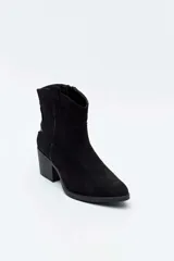 Bota corta de gamuza color negro, estilo texana, con taco cuadrado y puntera ligeramente perfilada. Presenta costuras decorativas en el empeine y tiradores laterales.
