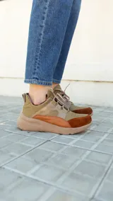 Championes deportivos de cuero en tonos marrón, tostado y marrón oscuro, con detalles de estampado animal print de leopardo en el lateral, suela gruesa blanca y cordones elásticos.