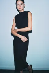 Vestido negro, largo, de cuello perkins y manga sisa, con detalle de espalda descubierta y bajo en línea evasé.