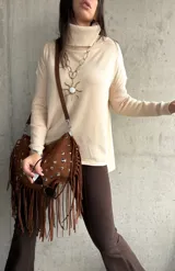 Polera de tejido de punto color beige, con cuello alto, mangas largas y aberturas laterales en el ruedo.