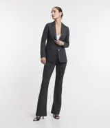 Blazer alargado color gris oscuro, con cuello solapa, bolsillos incorporados y cierre frontal con dos botones.