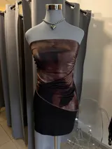 Top strapless de satén con diseño bicolor, presentando una parte superior con estampado abstracto en tonos marrones y una parte inferior negra con corte asimétrico.