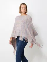 Poncho de tejido suave, color crudo con hilos multicolores que generan un efecto jaspeado en tonos pastel (rosa, celeste, lila). Presenta un diseño asimétrico con cuello redondo y terminación en flecos largos en el ruedo.