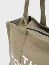 Bolso tipo tote de Marc Jacobs, confeccionado en lona resistente de color negro. Presenta el nombre del modelo estampado en blanco en la parte frontal y el logo de la marca debajo. Cuenta con doble asa superior para llevar al hombro o en la mano.