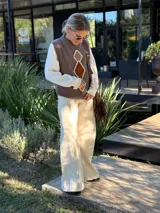 Chaleco tejido de punto en color chocolate, con cuello redondo y diseño sin mangas. Presenta un aplique frontal decorativo compuesto por tres figuras en forma de rombo en tonos tierra, bordeadas con hilo crudo.