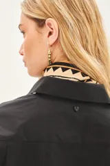 Camisa de popelina de algodón en color negro, con corte amplio, cuello clásico y cierre frontal con botones. Presenta un diseño versátil con botones en los laterales que permiten un ajuste cruzado.