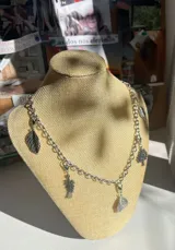 Collar plateado con cadena de eslabones y dijes colgantes con forma de hojas y árbol.