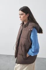 Chaleco puffer negro con diseño acolchado, capucha desmontable y cierre frontal. Cuenta con cordones ajustables en la cintura y bolsillos laterales.