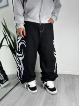 Pantalón baggy negro de corte ancho y relajado, con diseño tribal estampado en color blanco en los laterales y costuras en contraste.