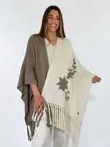 Ruana de punto bicolor, con un lado marrón y otro lado beige con detalle de bordado floral y flecos en los bordes inferiores.