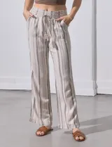 Pantalón largo de lino color beige con rayas verticales marrones. Tiene pretina ancha en punto smock con lazo ajustable, bolsillos verticales delanteros y bolsillos aplicados traseros.