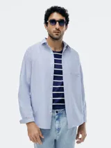 Camisa Oxford de manga larga en color celeste, con cuello clásico, cierre frontal de botones y bolsillo en el pecho.