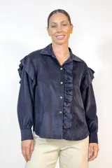 Camisa de pana fina color negro, con volados decorativos en los hombros y a lo largo de la botonadura frontal. Presenta cuello clásico, mangas largas con puños abotonados y botones dorados frontales.