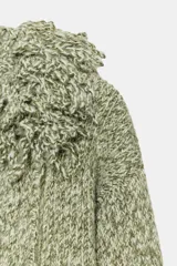 Chaqueta de punto de textura jaspeada en color verde, con cuello redondo adornado con flecos del mismo tejido, manga larga y cierre frontal con corchete metálico.