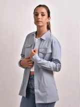 Sobre camisa celeste con cuello clásico, cierre frontal con botones a presión, dos bolsillos con solapa en el pecho y mangas largas con puños abotonados.