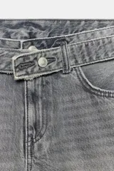 Bermuda de denim color gris con efecto acid wash, tiro medio, bolsillos delanteros y traseros, con detalle de cinturón del mismo tejido con hebilla y pliegues laterales. Cierre frontal con cremallera y botón metálico.