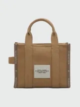 Bolso tipo tote Marc Jacobs modelo The Small Tote, color beige con detalles y texto en negro que dice "THE TOTE BAG MARC JACOBS". Cuenta con asas superiores y laterales para llevar en la mano o al hombro.