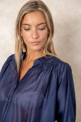 Camisa de organza blanca con cuello mao, diseño de manga larga tipo murciélago y cierre frontal con botones. Presenta un corte holgado y fluido.