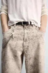 Pantalón de corte baggy fit confeccionado en tejido de algodón con efecto lavado y estampado abstracto en tonos beige y gris. Presenta diseño de cinco bolsillos, cierre frontal con cremallera y botón.