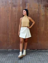 Falda corta tipo wrap de cuero color crudo, con diseño cruzado y ajuste mediante tiritas laterales.