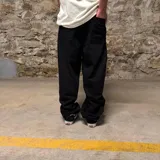 Pantalón de jean negro de corte super baggy, con múltiples bordados temáticos de automovilismo en las piernas.
