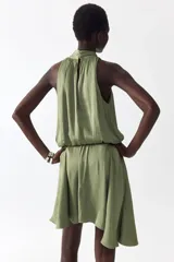 Vestido corto verde oliva con leve brillo, cuello halter elevado con frunces, cuerpo holgado con cintura elástica y falda corta de corte asimétrico.