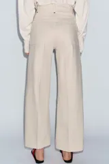 Jeans de tiro alto confeccionados en mezcla de algodón, con diseño de pierna ancha y costura marcada en el delantero. Presenta cintura con trabillas, cierre frontal con cremallera, botón y gancho metálico, y bolsillos de plastrón en la espalda.