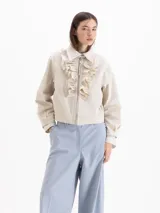 Campera bomber color beige, confeccionada en una mezcla de poliéster y algodón, con cuello camisero, cierre frontal con cremallera y volados superpuestos en la pechera.