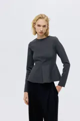 Blusa de manga larga confeccionada en punto grueso, con diseño entallado, escote redondo y cierre oculto en la espalda. Presenta costuras frontales que estilizan la figura y un detalle de peplum con vuelo en la cintura.