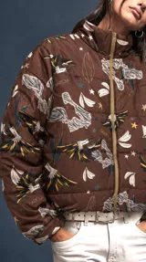 Campera puffer color marrón habano con estampado de loros, estrellas y elementos botánicos, cuello alto y cierre frontal.