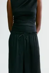 Pantalón holgado de satén negro, con piernas amplias, cintura elástica con cordón ajustable y bolsillos laterales.