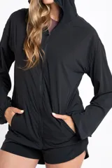 Campera deportiva de color negro con cierre frontal, capucha y mangas largas con puños elásticos. Presenta una textura ligera y un corte ajustado al cuerpo.