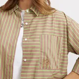 Camisa de corte oversize con diseño a rayas verticales en tonos marrón y verde neón. Presenta cuello clásico, cierre frontal con botones, mangas tres cuartos y un bolsillo frontal con el logo de la marca bordado.