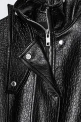 Chaqueta de corte oversize con acabado efecto piel. Presenta cuello alto, cierre frontal con cremallera y botones ocultos bajo solapa, bolsillos de plastrón con solapa en el delantero, mangas largas ajustables con trabillas y bajo ajustable con hebillas metálicas.