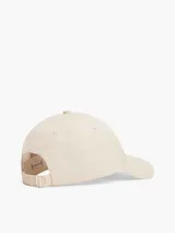 Gorra de béisbol color beige claro, confeccionada en algodón peinado. Presenta el logo de Tommy Hilfiger en dorado en el frente y hebilla metálica ajustable en la parte trasera.