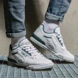 Championes Lacoste modelo M89, de diseño urbano y deportivo. Presentan una base de cuero blanco con perforaciones laterales para mayor ventilación, detalles en color verde oscuro en el cuello, logo de la marca y refuerzos, y una suela de goma gris con diseño texturizado.