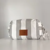 Neceser rectangular de tela a rayas verticales grises y blancas, con parche de cuero marrón con logo de la marca.