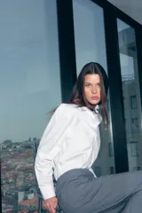 Camisa blanca de algodón con corte holgado, cuello clásico y botones frontales. Presenta mangas largas con puños abotonados y bajo redondeado.