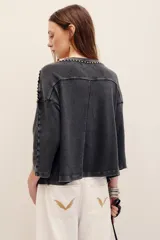 Remera de algodón negro con efecto deslavado, cuello redondo y mangas cortas. Presenta aplicaciones de tachas metálicas en el escote, hombros y a lo largo del frente.
