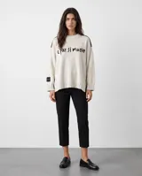 Sweater oversized crudo de tejido de punto, con hombros caídos y mangas largas. Presenta líneas negras en contraste en los hombros, bordado artesanal con la frase "e pur si muove" en el frente y aberturas laterales en el dobladillo.