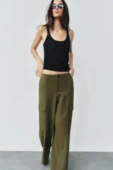 Pantalón cargo de tiro medio, color verde militar, con corte recto y bolsillos laterales de plastrón con solapa. Presenta detalles de nervios frontales y cierre con cremallera y gancho metálico.