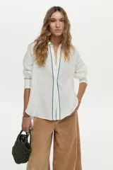 Camisa de lino blanca con detalles de bordado azul en el frente, espalda y puños, mangas largas y corte holgado.