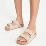Sandalias Melissa modelo Cozy Slide M-Lover, en color beige con suela marrón. Presentan dos tiras superiores con hebillas ajustables y tiras de tela con la marca estampada.